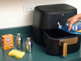 Person cleaning an air fryer basket with a sponge and soapy water