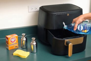 Person cleaning an air fryer basket with a sponge and soapy water